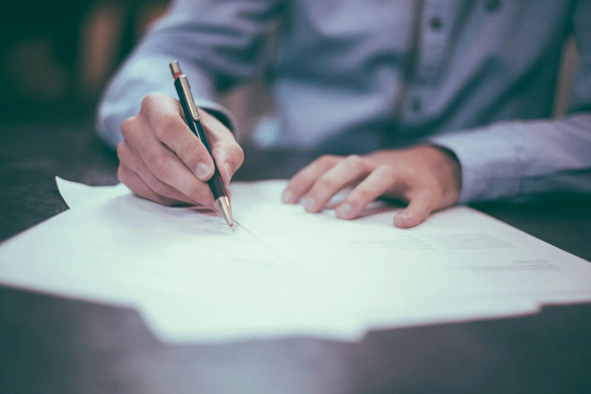 Dłoń z długopisem podpisująca papierowy protokół serwisowy na biurku